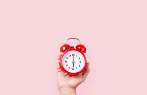 Fotografie einer roten Uhr vor rosa Hintergrund
