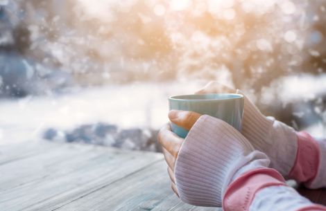 Frau sitzt eingemummelt in Winterlandschaft mit einer Tasse Tee.