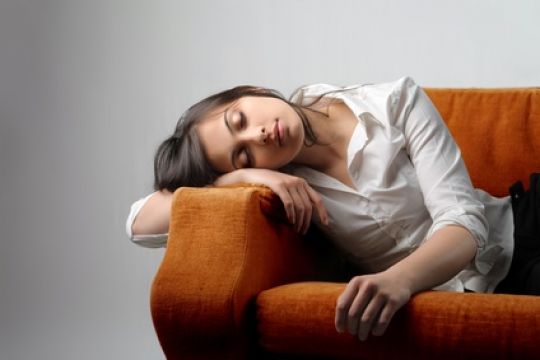 Junge Frau liegt schlafend auf dem Sofa und leidet unter Abgeschlagenheit.