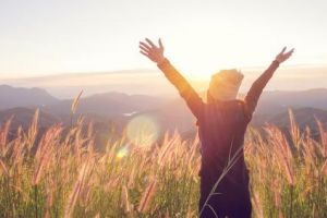 Frau steh vor Gebirge im Sonnenschein und breitet Arme aus