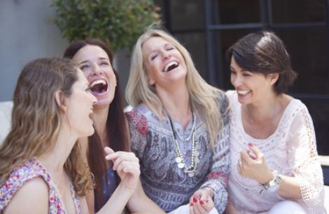 Vier Frauen sitzen fröhlich auf dem Sofa und lachen ausgelassen.