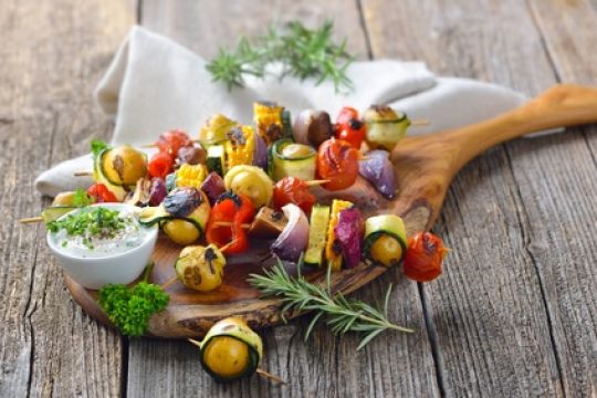 Grillsaison: Gemüse-Spieße auf einem Holzbrett mit Quark-Dip. 