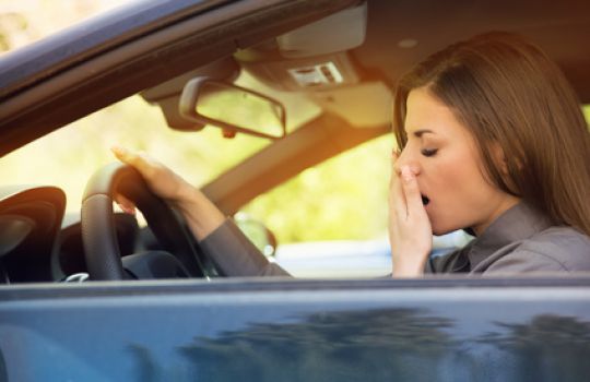 Junge Frau fährt Auto und gähnt - ausgeprägte Tagesschläfrigkeit ist gefährlich.