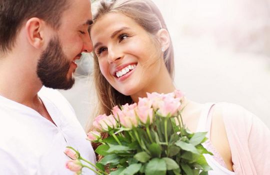 Valentinstag: Frau mit Rosenstrauß lächelt ihren Liebsten an.