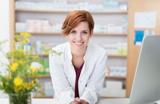 Apothekerin mit Heilpflanzen-Strauß steht lächelnd an der Theke.