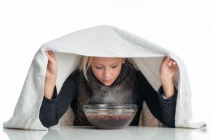 Frau inhaliert über Wasserschüssel, um Erkältung und Sinusitis zu behandeln.