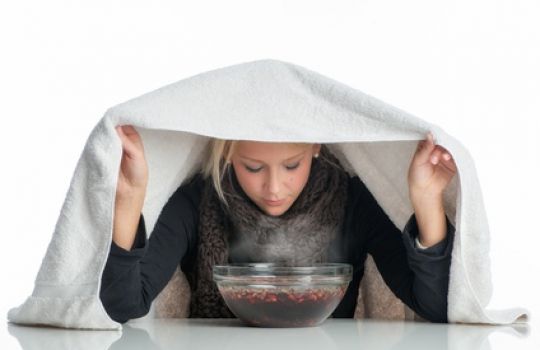 Frau inhaliert über Wasserschüssel, um Erkältung und Sinusitis zu behandeln.