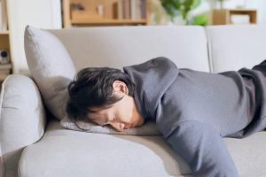 Mann liegt abgeschlafft bäuchlings auf einem Sofa