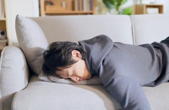 Mann liegt abgeschlafft bäuchlings auf einem Sofa