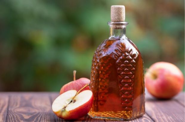 Apfelessig in einer schönen Flasche steht mit Äpfeln auf einem Holztisch. 