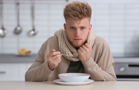 Erkälteter, junger Mann mit Schal löffelt eine Hühnersuppe.