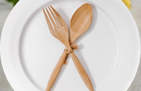 Gabel und Löffel aus Holz auf Teller überkreuzt