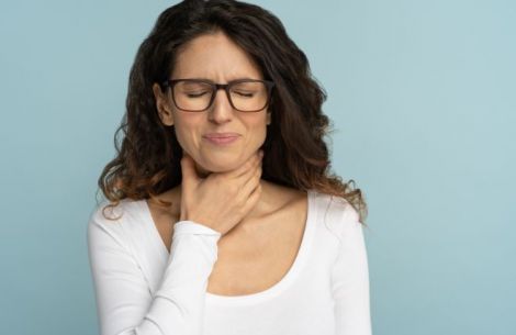 Frau fasst sich and en hals, schmerzvoller Gesichtsausdruck