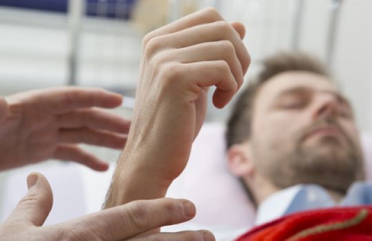 Ein Hypnosepatient hat die Augen geschlossen und erhebt seine Faust, zwei Hände greifen nach dem Handgelenk.